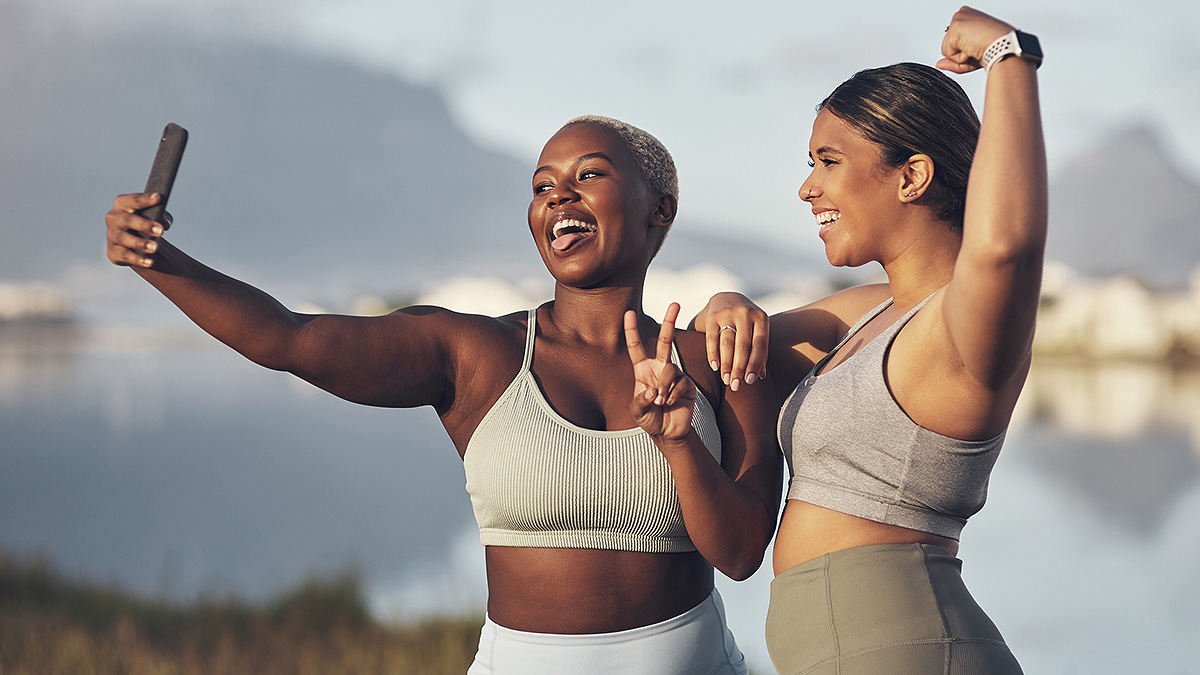 An African American man and a Latina woman pose with a peace sign and flexed bicep for a happy selfie.