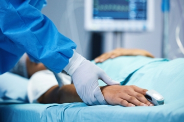 Close-up of patient on stretcher's right arm with gloved hand of doctor gently holding patient's wrist.